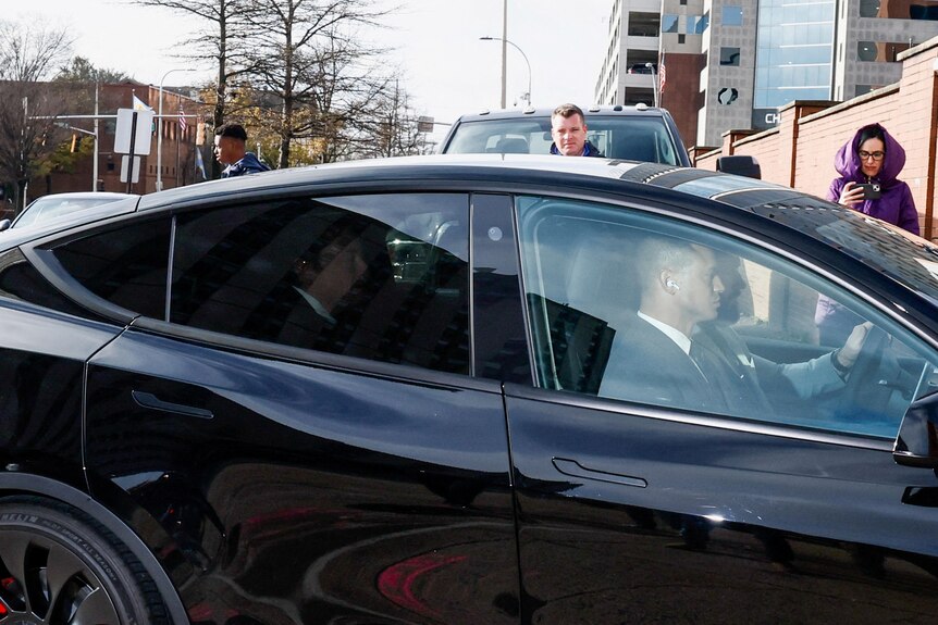 Elon Musk seen through tinted windows in the back seat of a Tesla., 