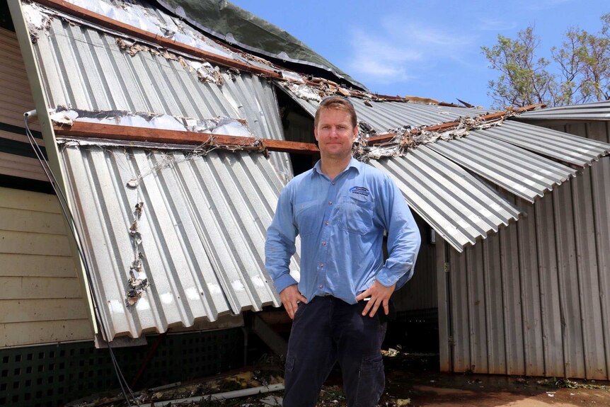 A man stands in front of his home, which has had the roof ripped off.