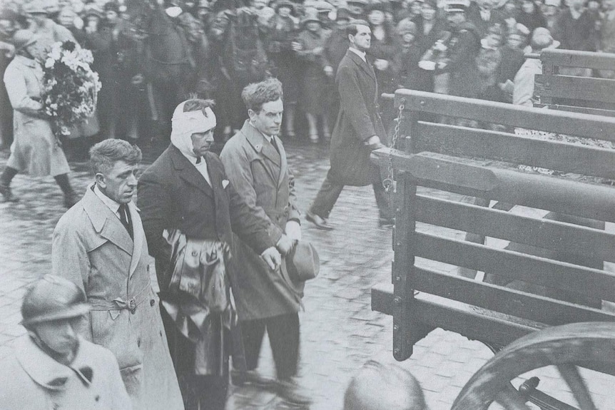 Black and white photo of injured people walking in past crowd.