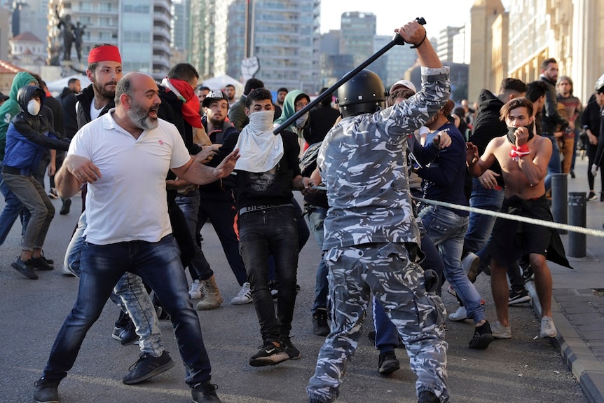 Riot police swing batons as anti-government protesters clash on a road.