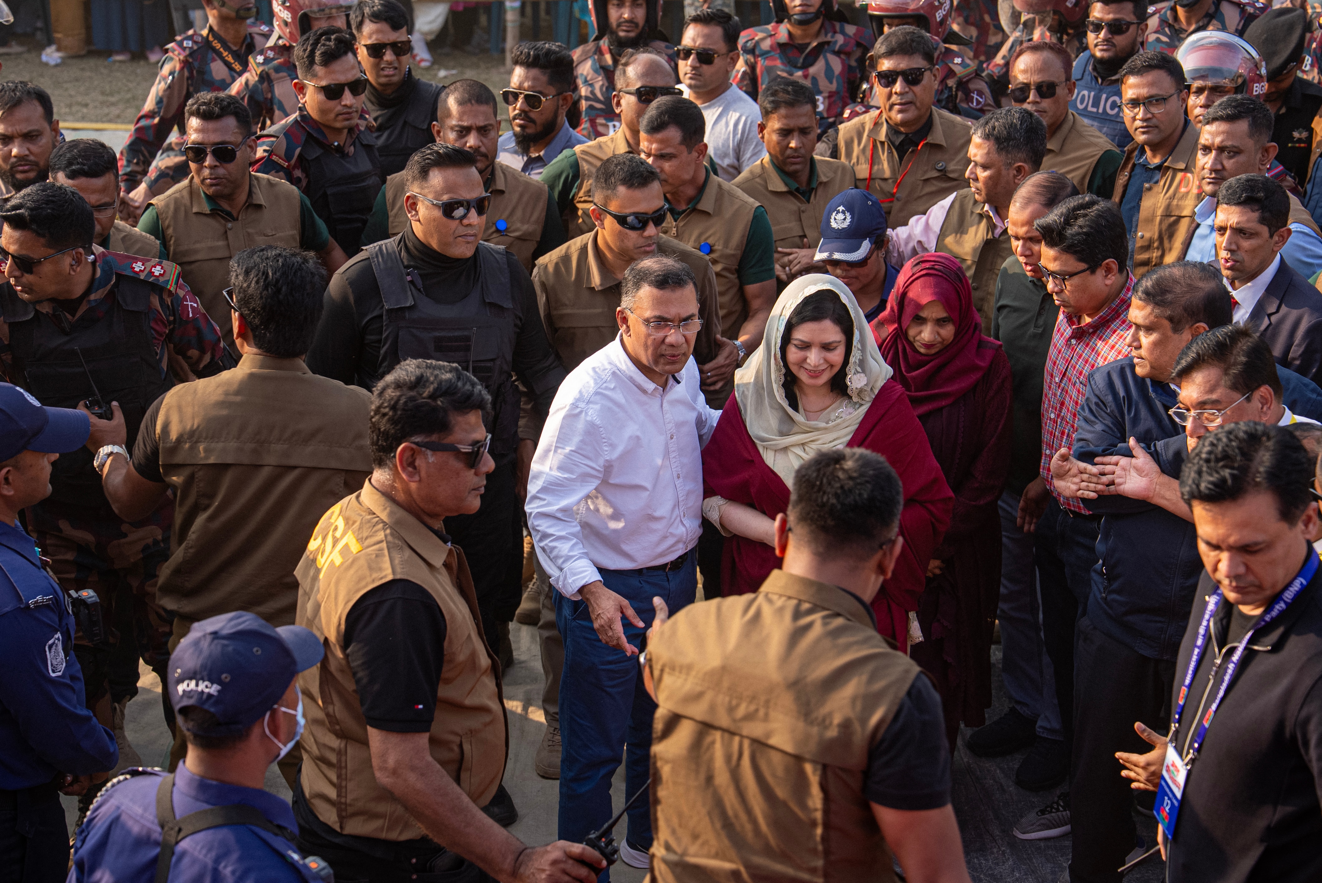 A Bangladesh man smiles and waves among a throng of people on a street.