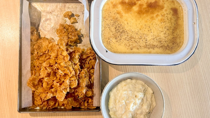 A bol of rice pudding next two a baking dish of baked custard and a tray of honey-coated cornflakes.