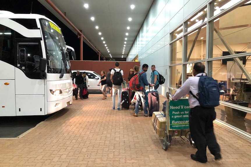 Passengers queue to board a coach bus.
