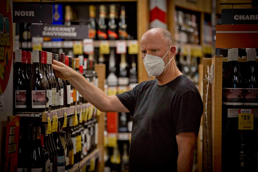 A man wearing a face mask reaches for a bottle of wine at a bottle shop in inner Sydney.