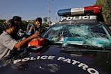 Police officer receives first aid beside police vehicle with smashed front window.
