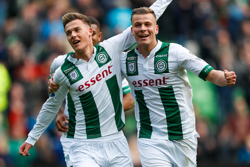 Two male soccer players wearing white and green stripes celebrate