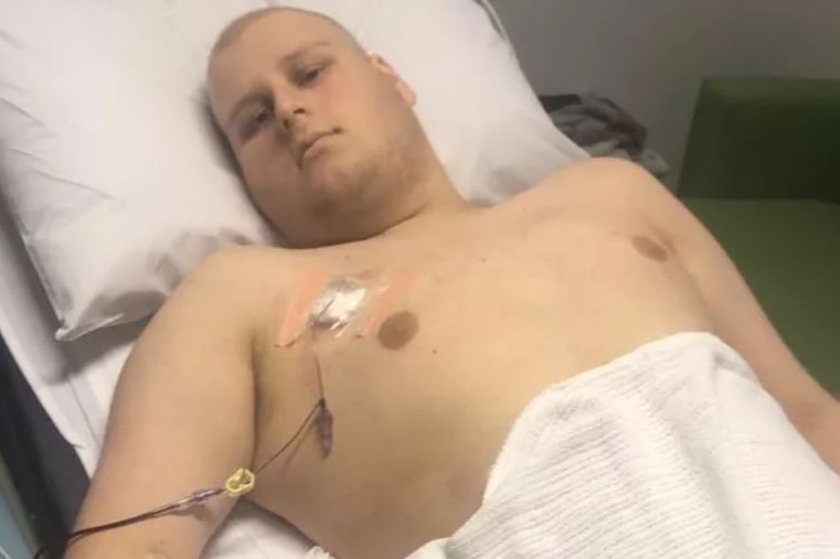 A teenager lies in a hospital bed with a tube attached to his chest