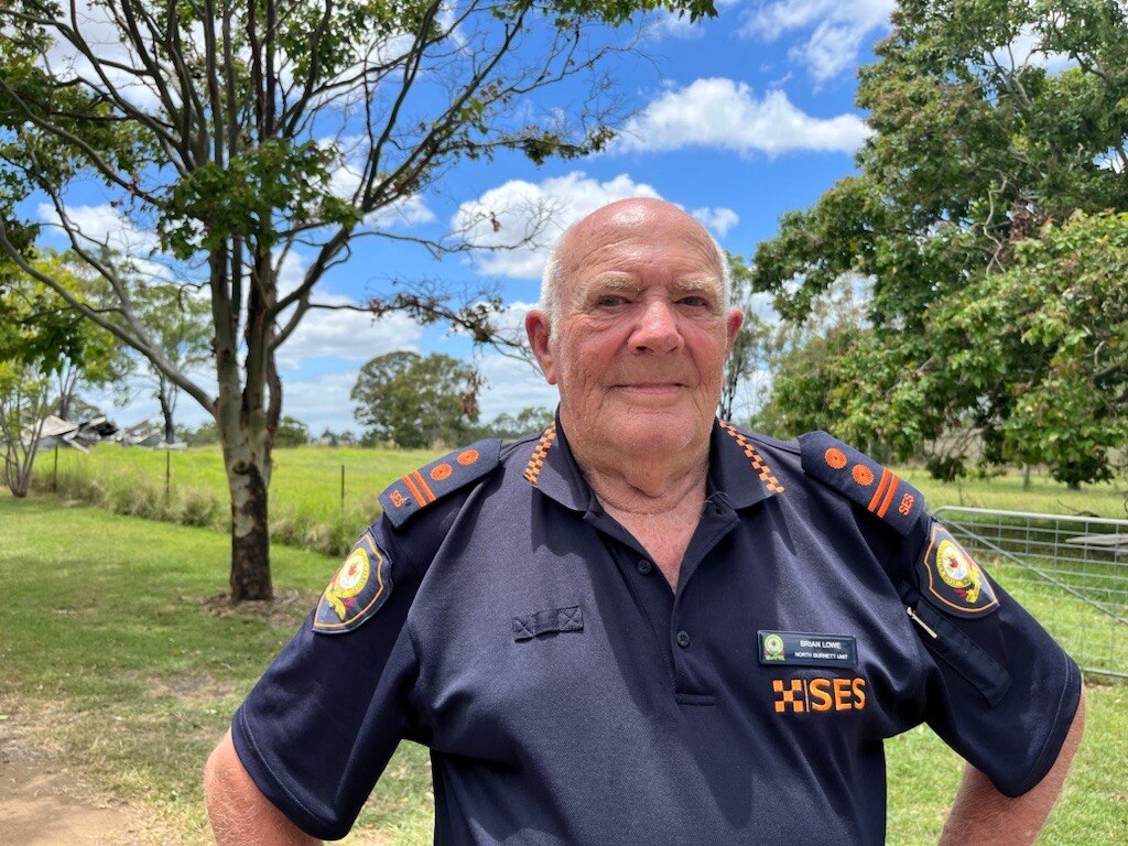 A man in an SES uniform looks at the camera with his hands on his hips, green paddock behind