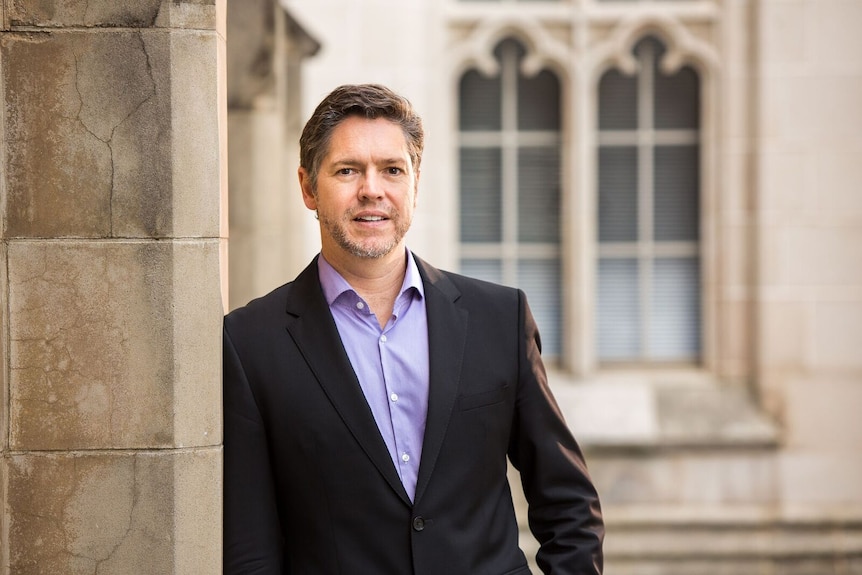 Nicholas Reece stands leaning against a brick wall