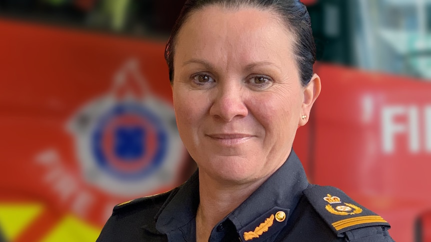 A dark-haired woman in uniform stands in front of a fire truck.