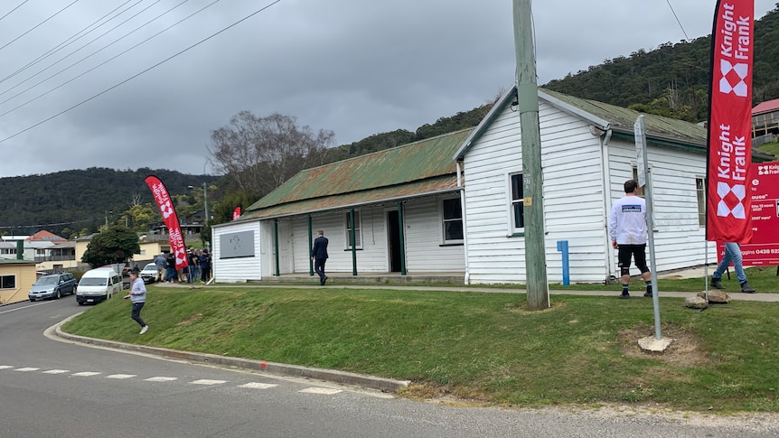 The front of an old house as people walk around it.