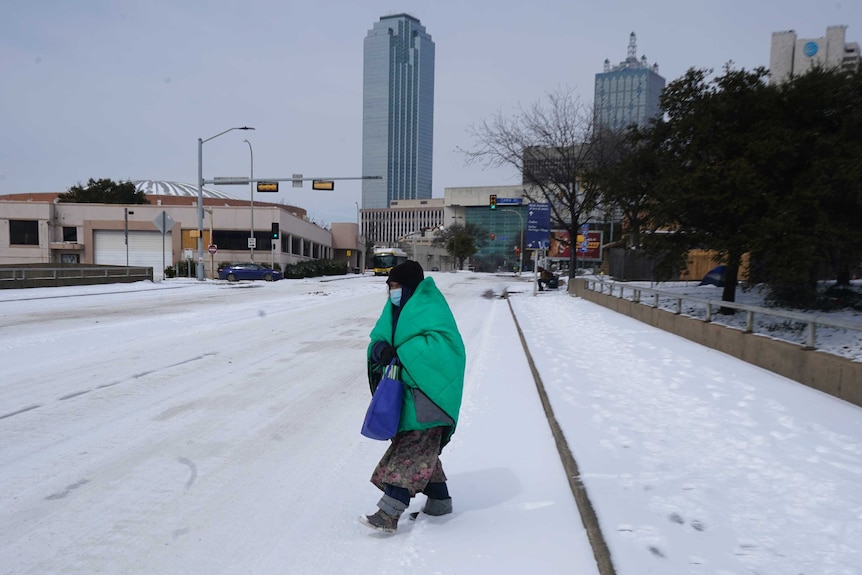 A woman wrapped in a blanket crosses a street covered in snow