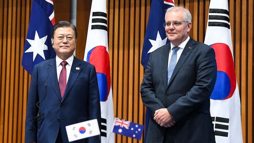Scott Morrison and Moon Jae-in stand in front of Australian and South Korean flags. 