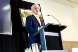 Malcolm Turnbull speaks at a podium, with the Closing the Gap projected onto a screen next to him.