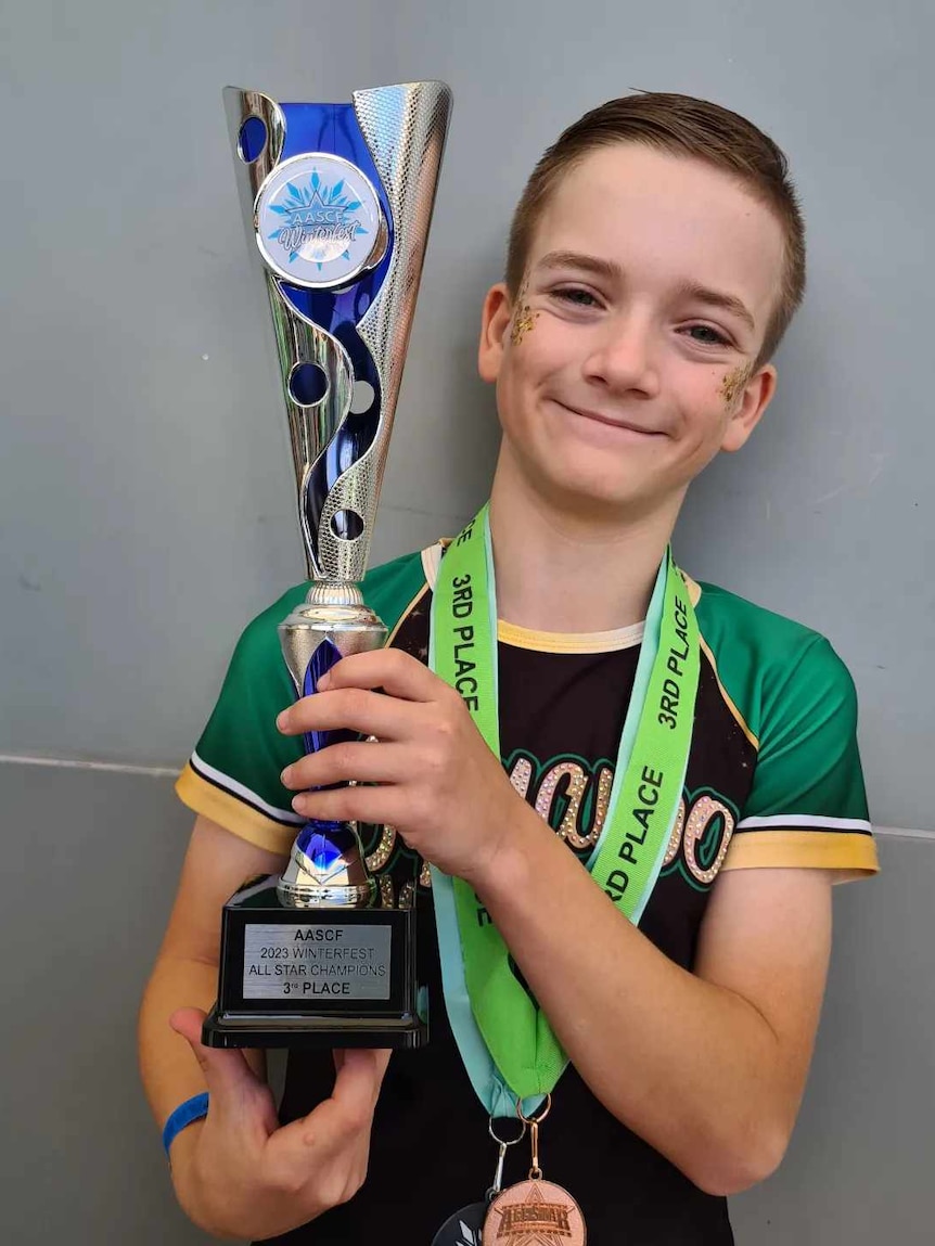 Young boy holding up a trophy smiling in his green and balck lycra sports uniform 