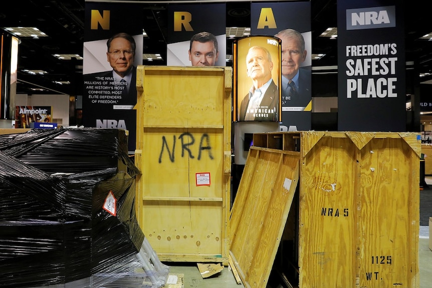 Shipping containers rest in front of images of National Rifle Association (NRA) leadership.