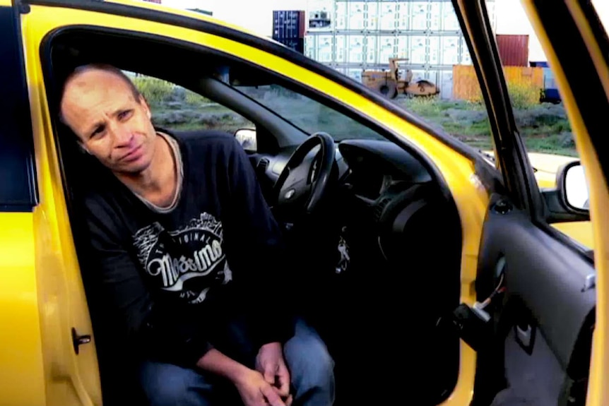Man in jeans and sweatshirt sits in yellow ute.
