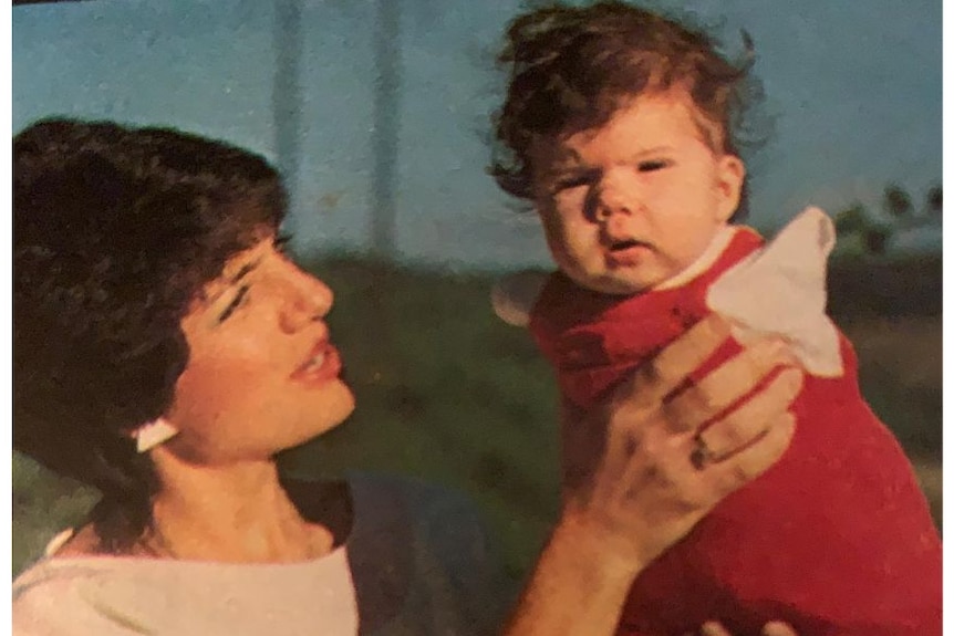 An old photo of a brunette woman holding a young girl baby with no arms.