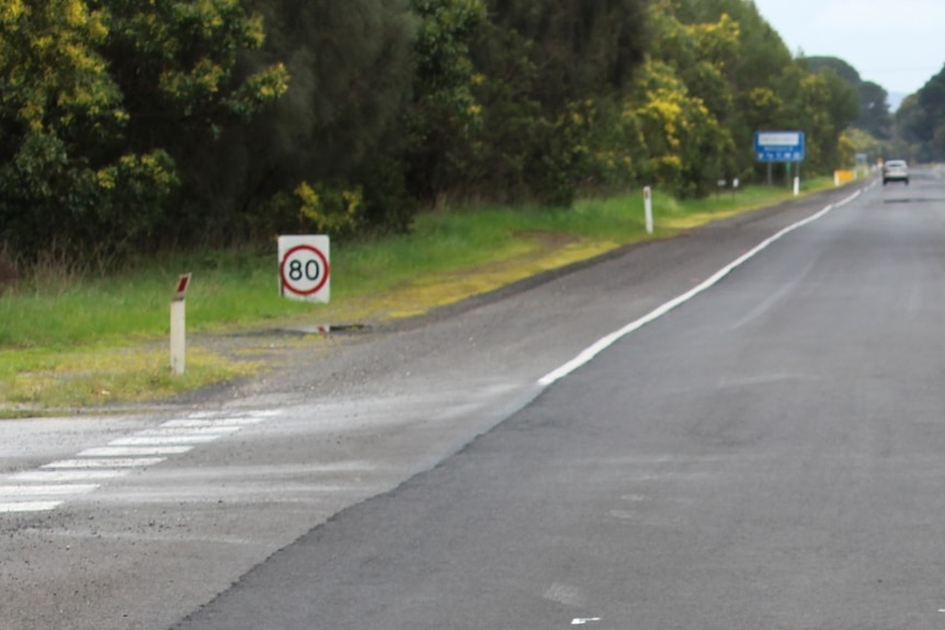 wide shot of road with pot holes and 80km/h an hour sign 