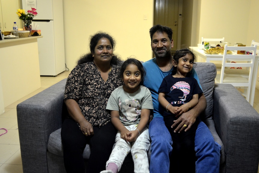 A Tamil family sits on a couch together, the dinner table in the background