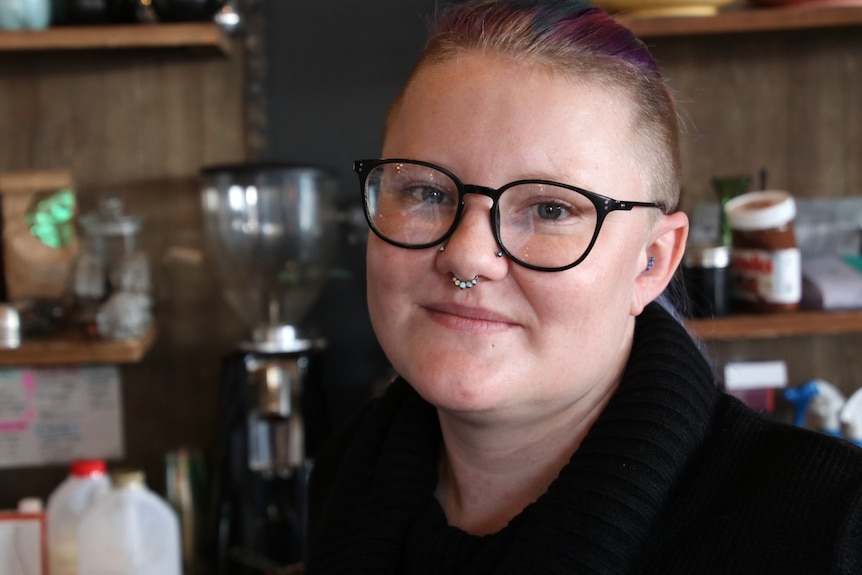 A close-up shot of a woman with black-rimmed spectacles on in a cafe.