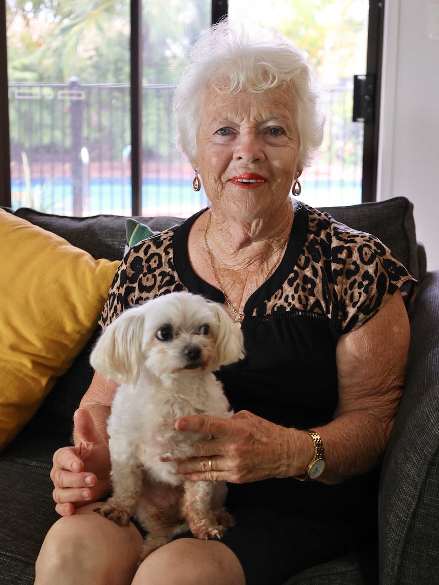 A woman sitting on a chair smiling with a dog in her lap.