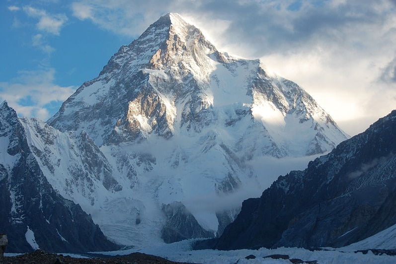 K2 appears in front of a blue sky with sun and some cloud cover