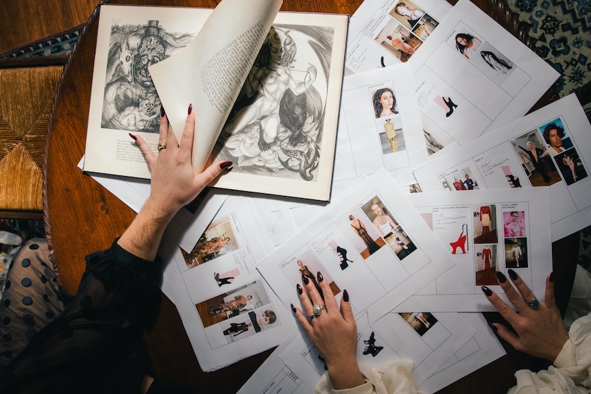 A series of designs sketched on paper with photos of models are splayed across a table.