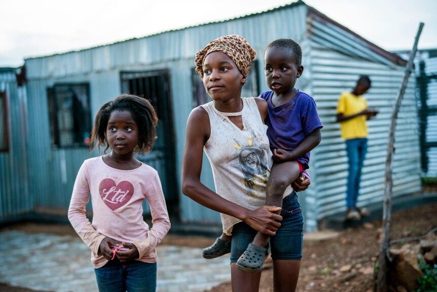 A teenaged girl holds a small boy on her hip while a little girl stands next to her 