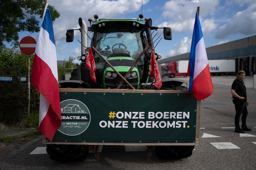 A tractor with two Dutch flags and a sign saying 'Our Farmers, Our Future' in front of a distribution centre.