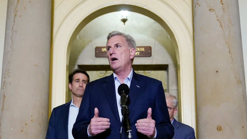 Kevin McCarthy wears an open-neck shirt and jacket as he speaks at a microphone