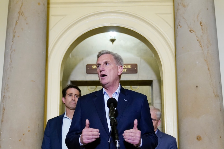 Kevin McCarthy wears an open-neck shirt and jacket as he speaks at a microphone