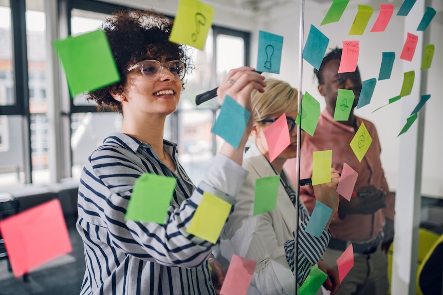 Young diverse office workers put post-it notes on a glass wall.