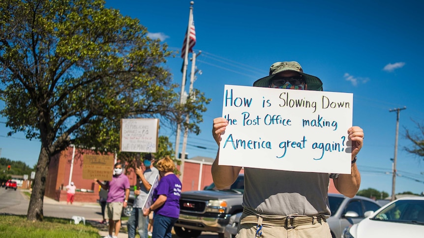 A protester holds a sign saying: How is slowing down the post office making America great again?