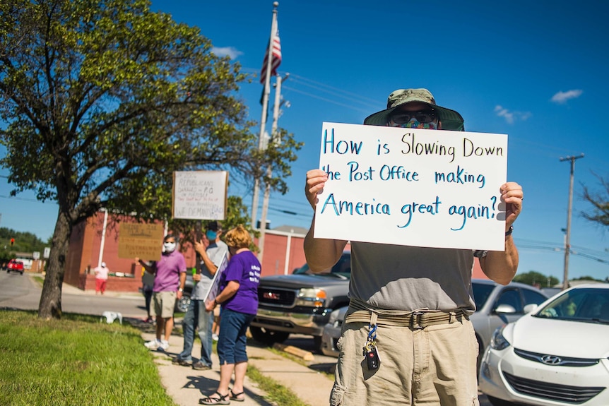 A protester holds a sign saying: How is slowing down the post office making America great again?