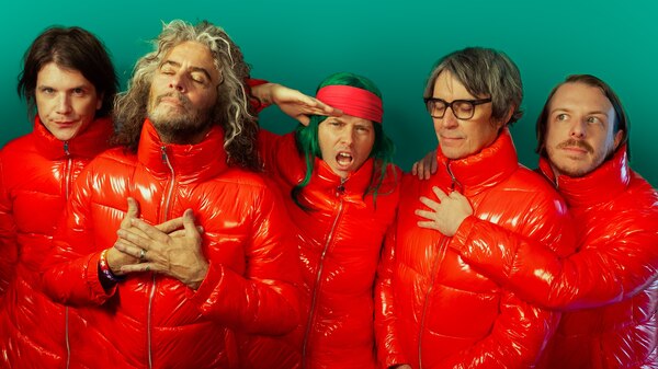 Five men in red puffer jackets make silly poses against green backdrop