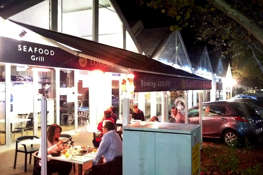 Diners sit out the front of restaurants at night.