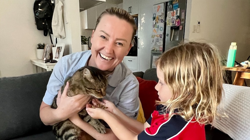 A cat bing cuddled by a woman and fed by her young son.