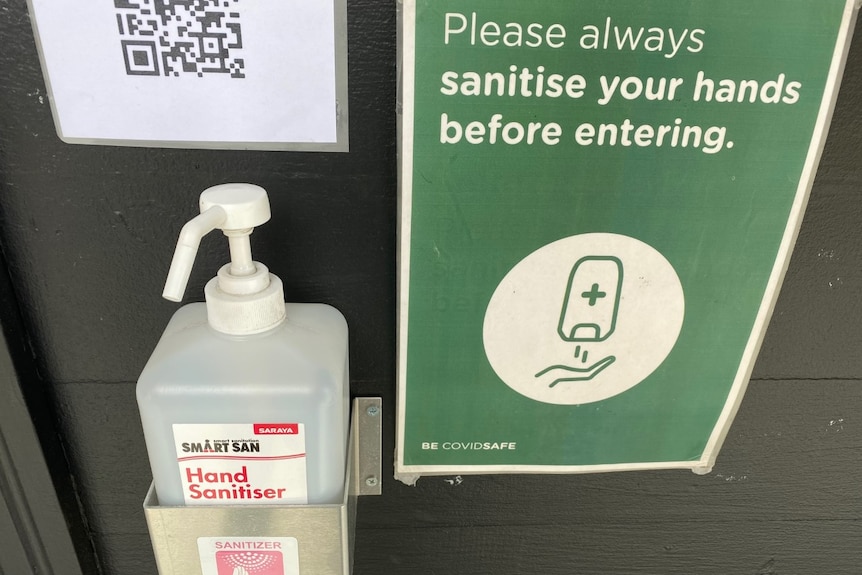 A close-up shot of hand sanitiser and a QR code outside a cafe in Hobart's CBD.