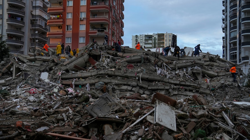 People and emergency teams search for people in a destroyed building in Adana