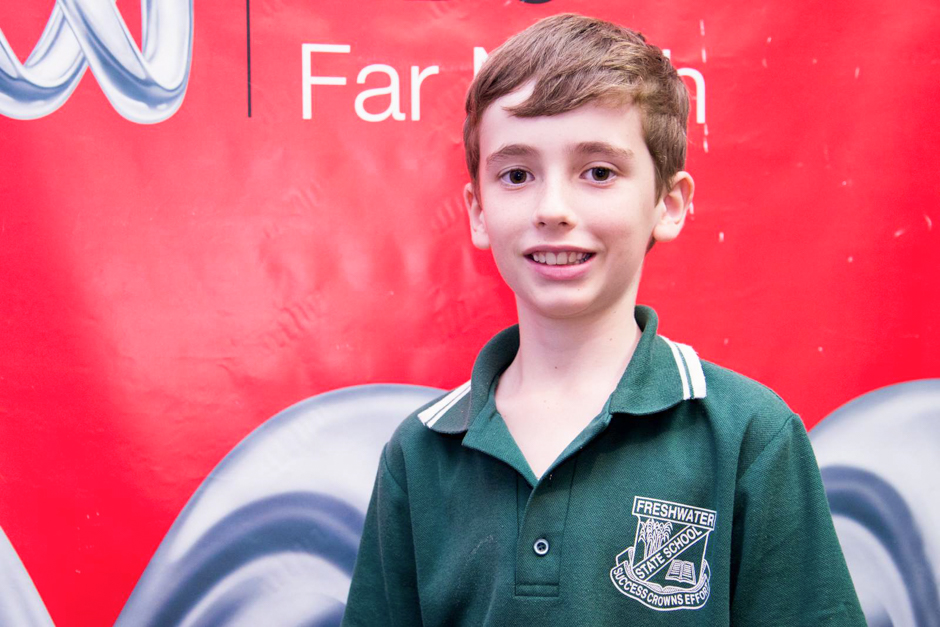 A year six boy stands in front of a bright red banner.