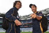 Tony Armstrong and Eddie Betts, wearing Australian training tracksuits, smile and point at the camera