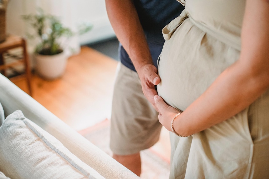 Pregnant woman and her partner place their hands on her belly.