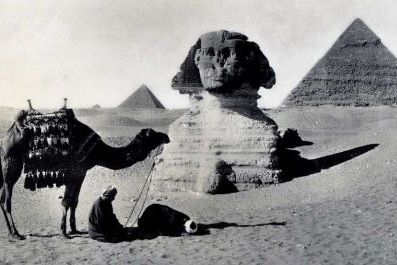 A historical photo of an Egyptian pyramid, sphinx and camel. 