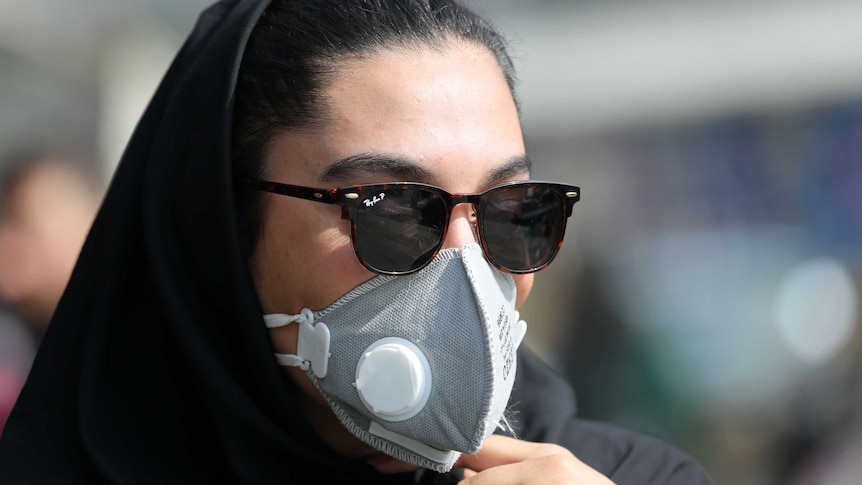 A woman wears a black medical mask.