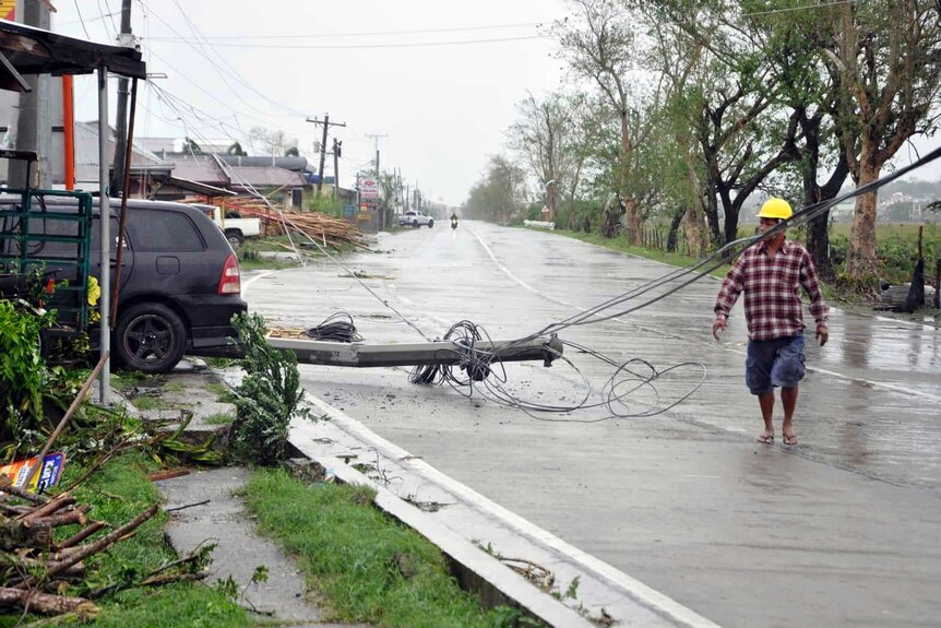 A man wearing a hard helmet walks along a street ravaged by the typhoon, including destroyed power lines and damaged buildings.