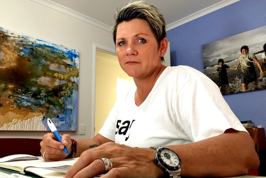 Woman sitting at a desk looking down at the camera while holding a pen.