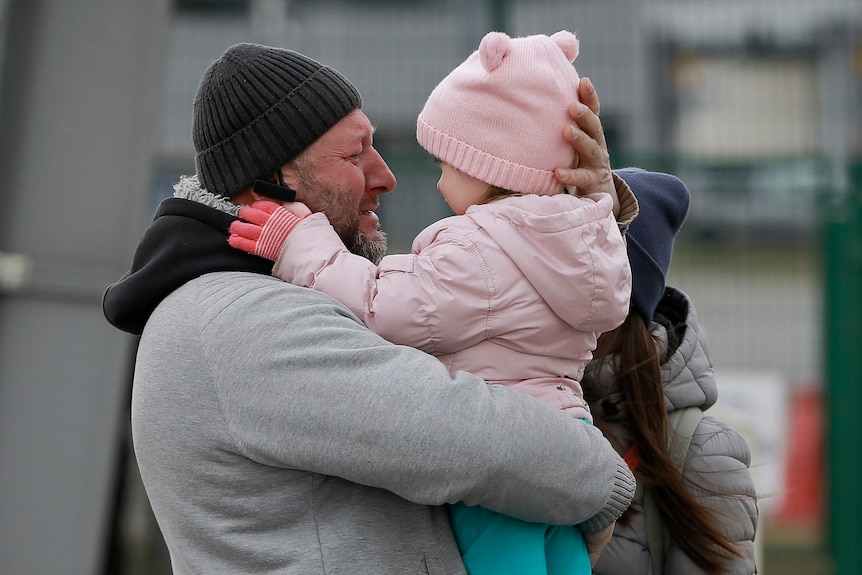 A father holds a small child in pink jacket.