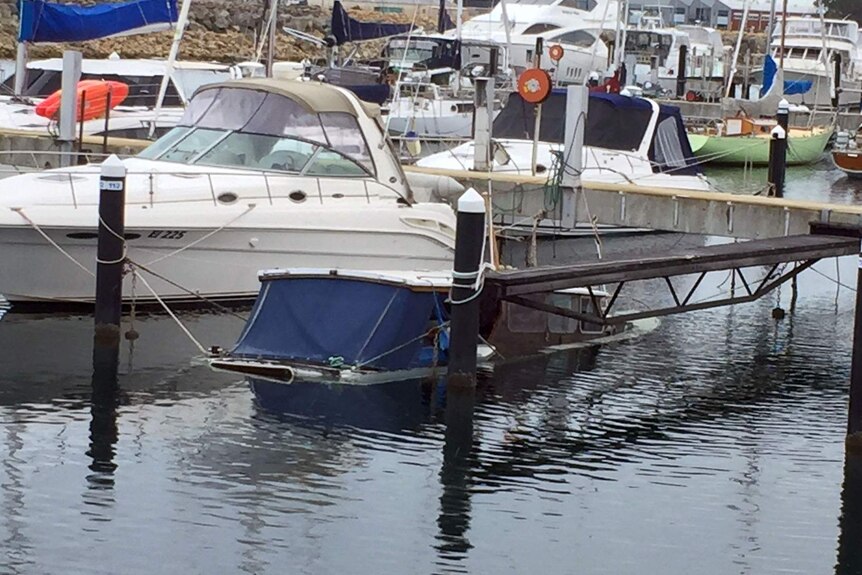 A boat sits half-underwater in its mooring at a marina.