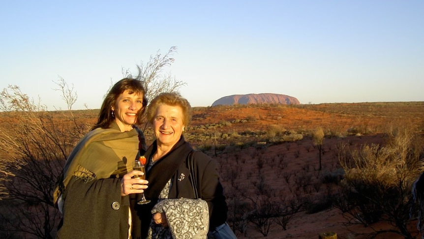 Elderly woman with her daughter standing with Uluru in the background.